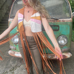 A woman wearing the camel Retro Sunburst Suede Color Block Long Fringe Faux Vest and holding out the fringe pieces.