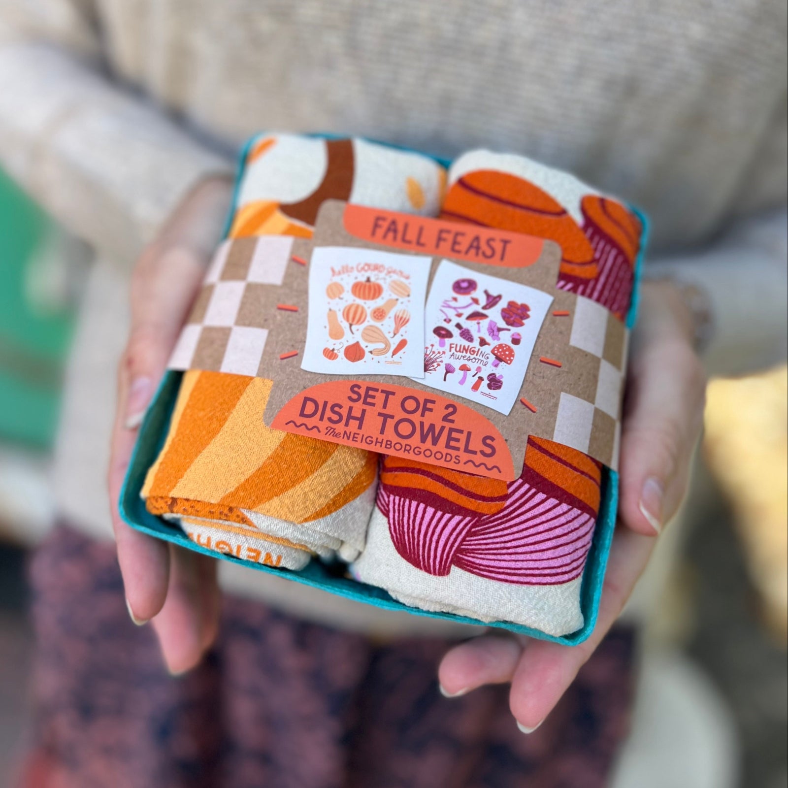 Someone holding the Fall Feast Tea Towel Set of 2 in front of themselves.