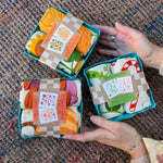 Three of the Tea Towel Sets from The Neighborgoods on a woven background.