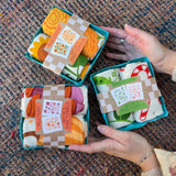 Three of the Tea Towel Sets from The Neighborgoods on a woven background.