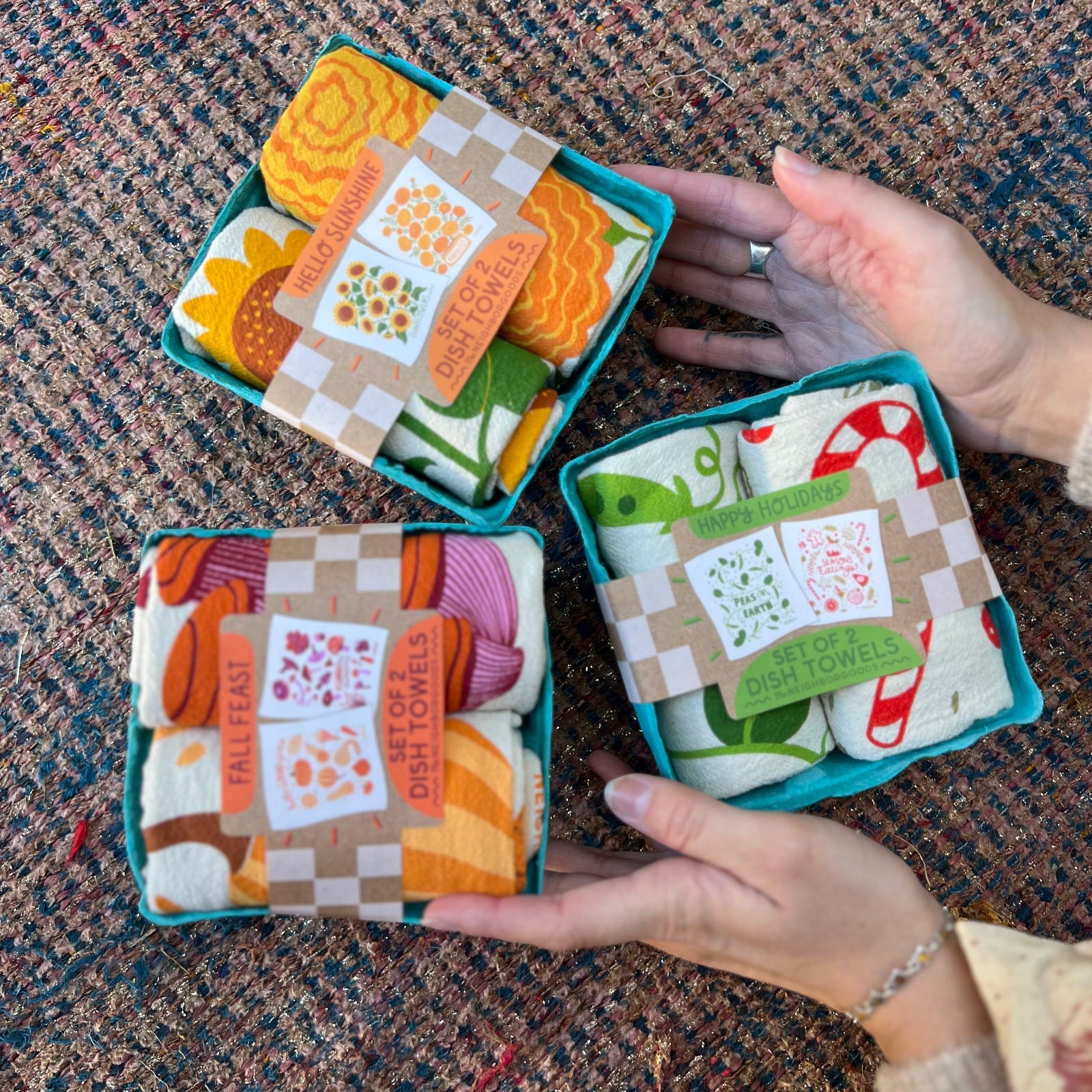 Three of the Tea Towel Sets from The Neighborgoods on a woven background.