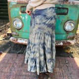 Someone wearing the indigo Tie Dye Gauze Cotton Skirt with a beige sweater in front of a vintage teal Volkswagen bus. Showing off the side.