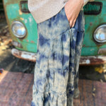 Someone wearing the indigo Tie Dye Gauze Cotton Skirt with a beige sweater in front of a vintage teal Volkswagen bus. Showing off the side.