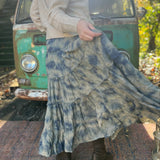 Someone wearing the indigo Tie Dye Gauze Cotton Skirt with a beige sweater in front of a vintage teal Volkswagen bus. Showing off the back.