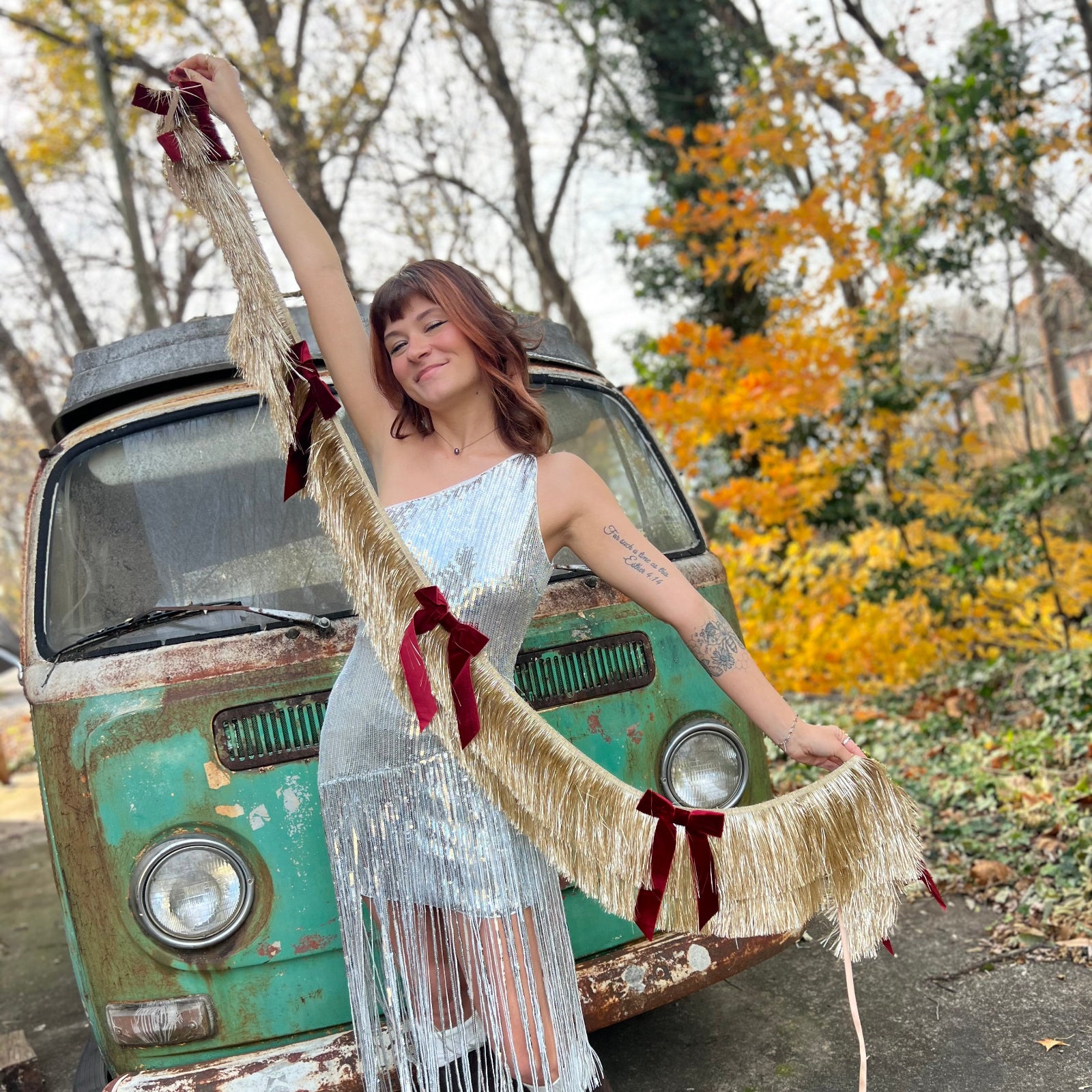 Someone holding the Gilded Bow Gold Layered Fringe Banner in front of a vintage teal Volkswagen bus.
