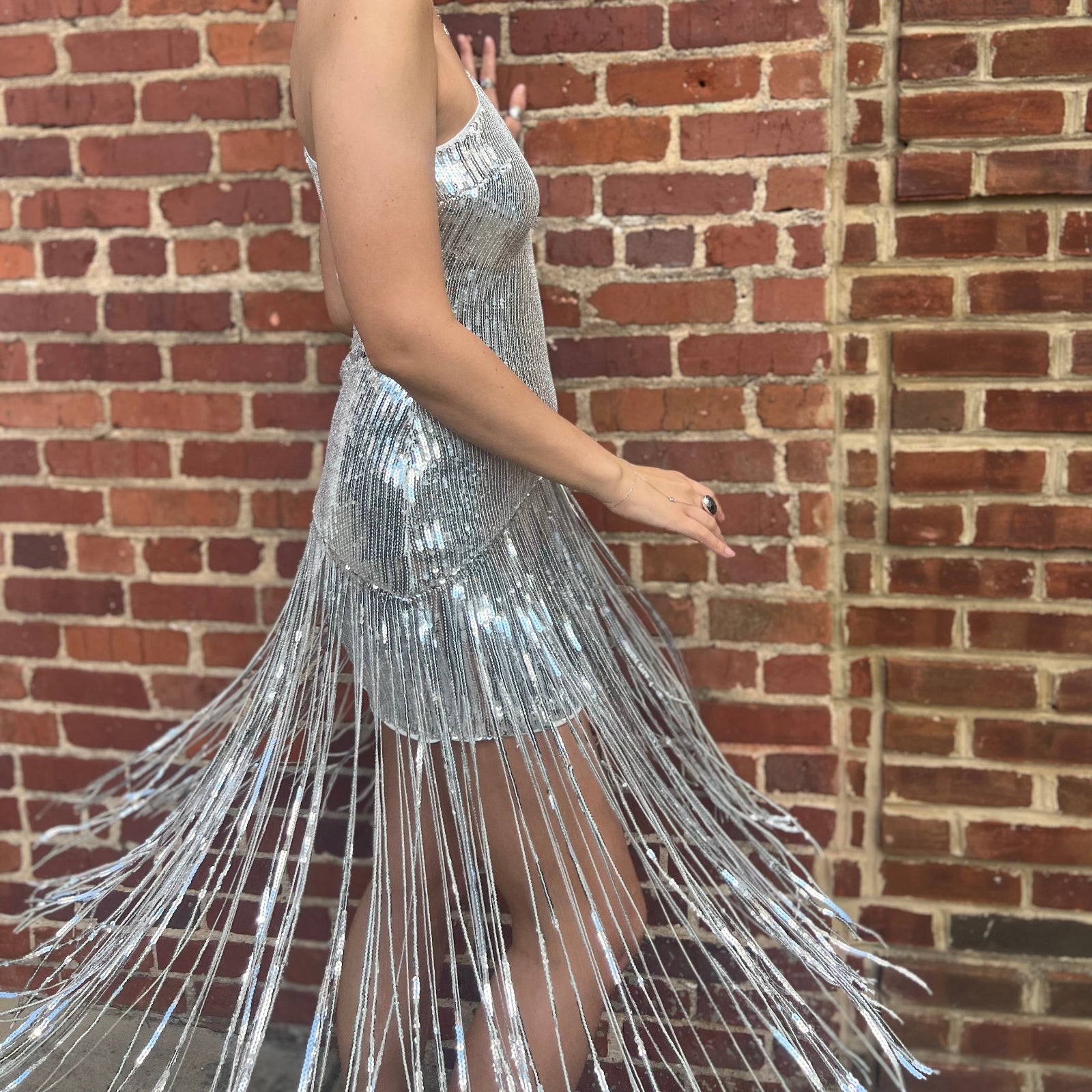 A woman wearing the Silver Sequin Disco Dress in front of a brick building.