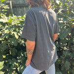 A woman wearing the Saja Boys Kpop Demon Hunters Inspired Cotton Tee with jeans in front of greenery, showing off the side.