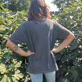 A woman wearing the Saja Boys Kpop Demon Hunters Inspired Cotton Tee with jeans in front of greenery, showing off the back.