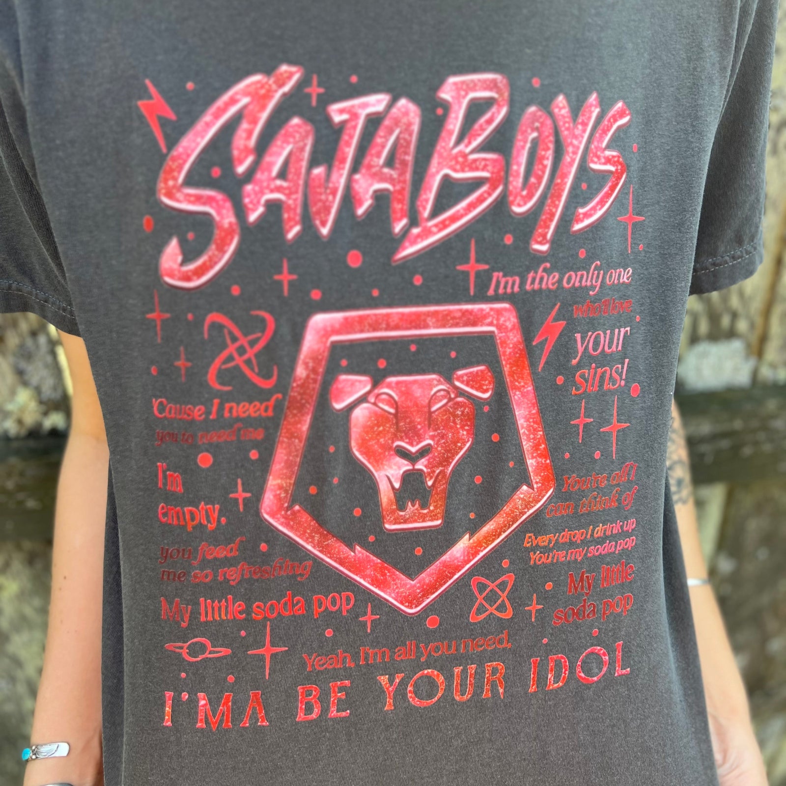 A woman wearing the Saja Boys Kpop Demon Hunters Inspired Cotton Tee with jeans in front of a wooden fence.