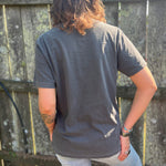 A woman wearing the Huntrix Kpop Demon Hunters Inspired Cotton Tee with jeans in front of a wooden fence, showing off the back.