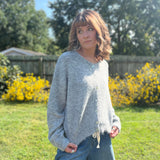 A woman wearing the heather gray Knit Round Neck Sweater Cardigan Top with jeans in front of some greenery.