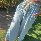 A woman wearing the light wash Denim Drawstring Waist Band Wide Leg Pants with a cream crocheted top.