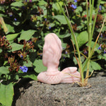 Pink stone sculpture of a hand on a rock with greenery and flowers in the background