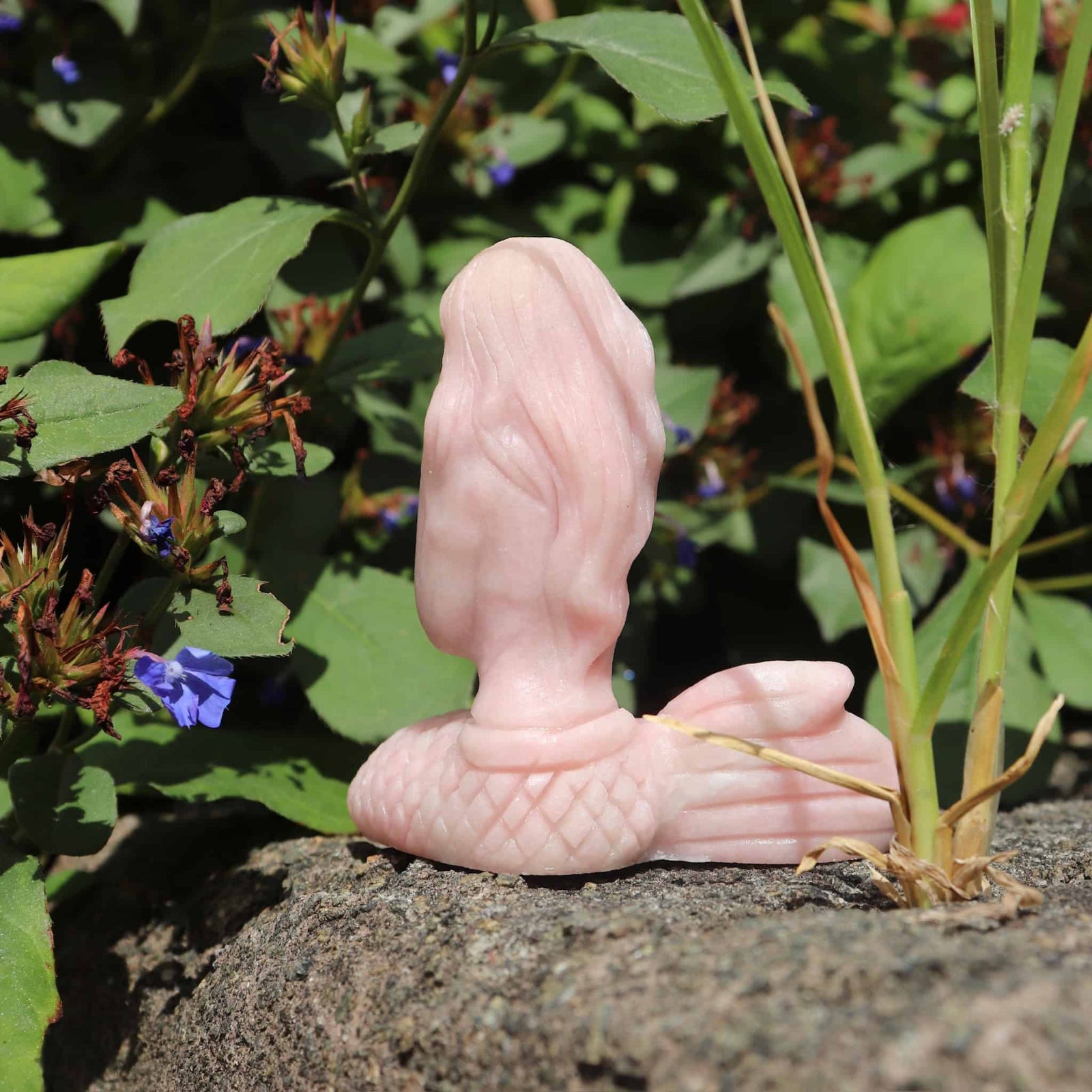 Pink opal crystal mermaid sculpture of a foot on a natural background with plants