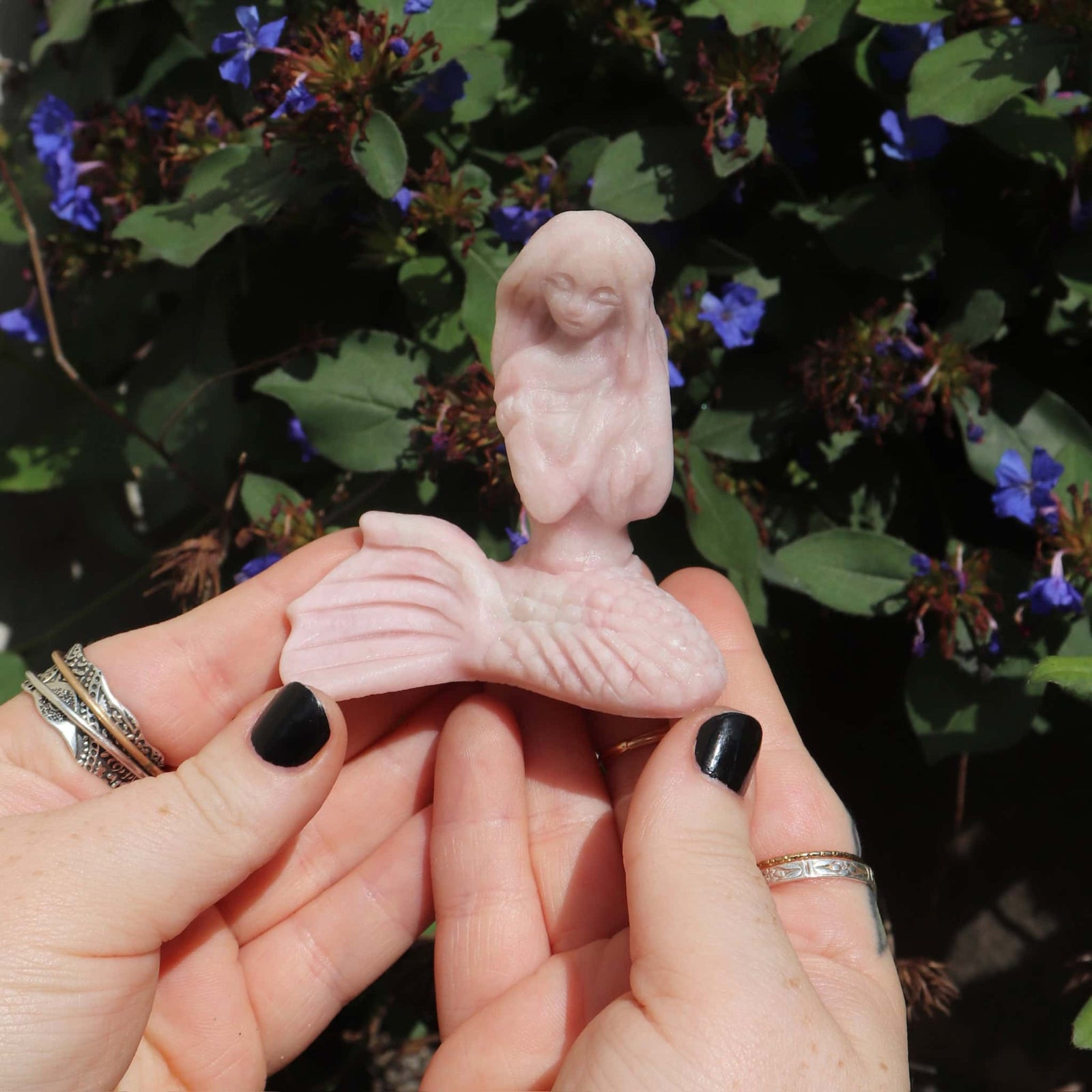 Pink opal crystal mermaid sculpture of a bird held between hands with a natural background