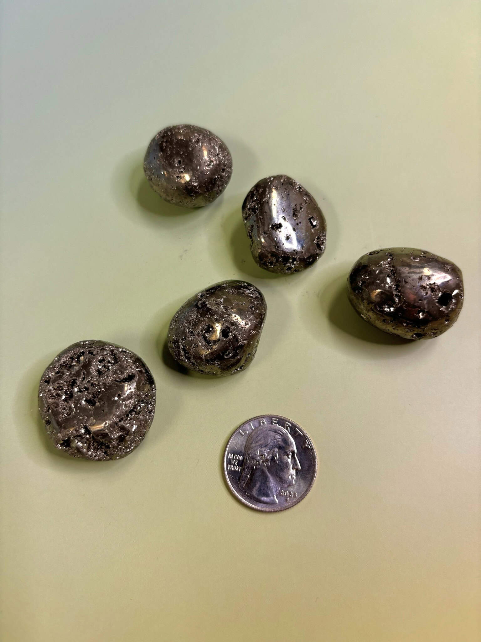 Pyrite Crystal Tumbled Stone on greenish background with quarter for size reference