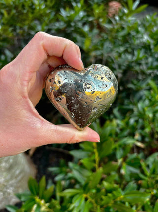 pyrite crystal heart in front of a green bush