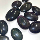 Polished rainbow obsidian palm stones reflecting light to reveal hidden color bands
