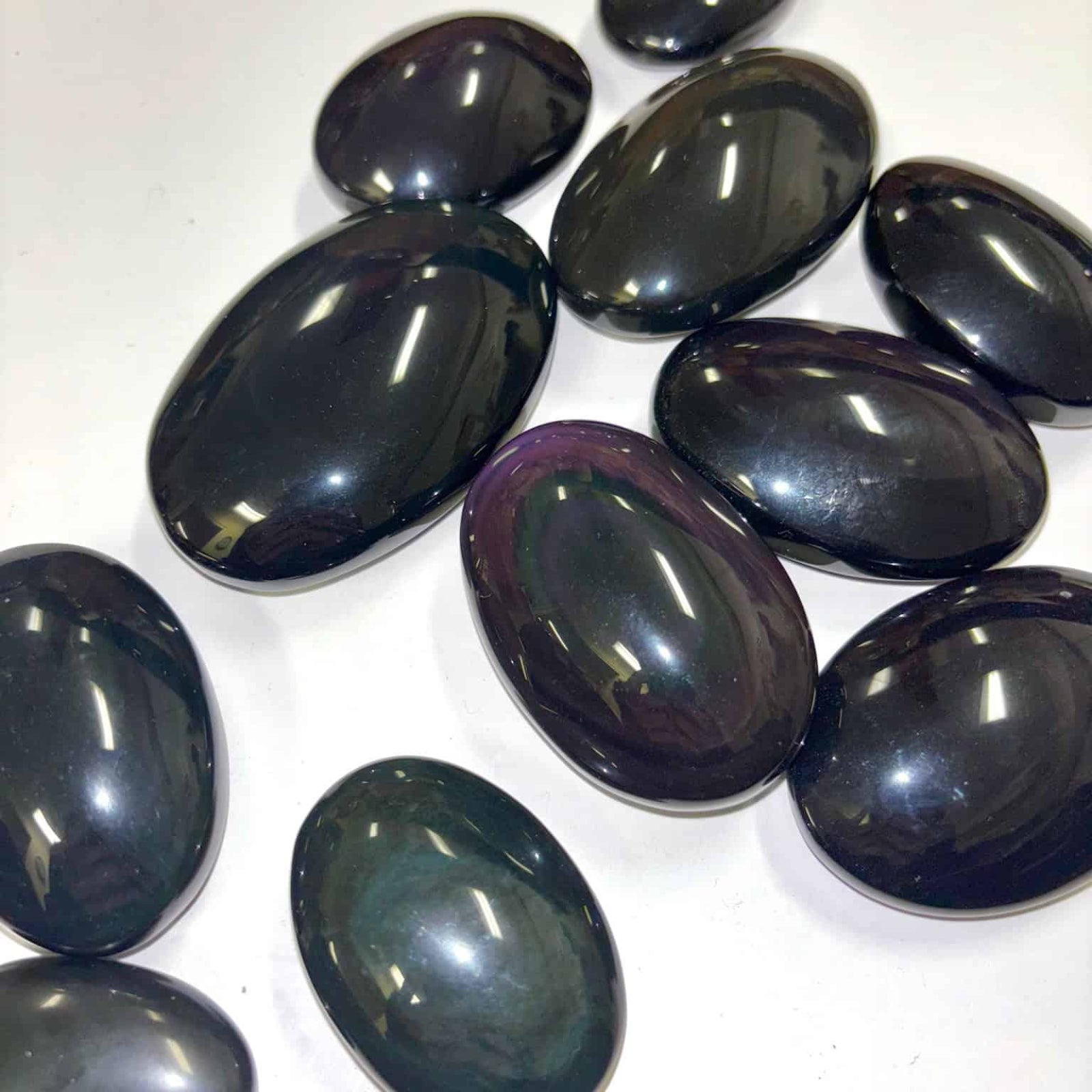 Polished rainbow obsidian palm stones reflecting light to reveal hidden color bands