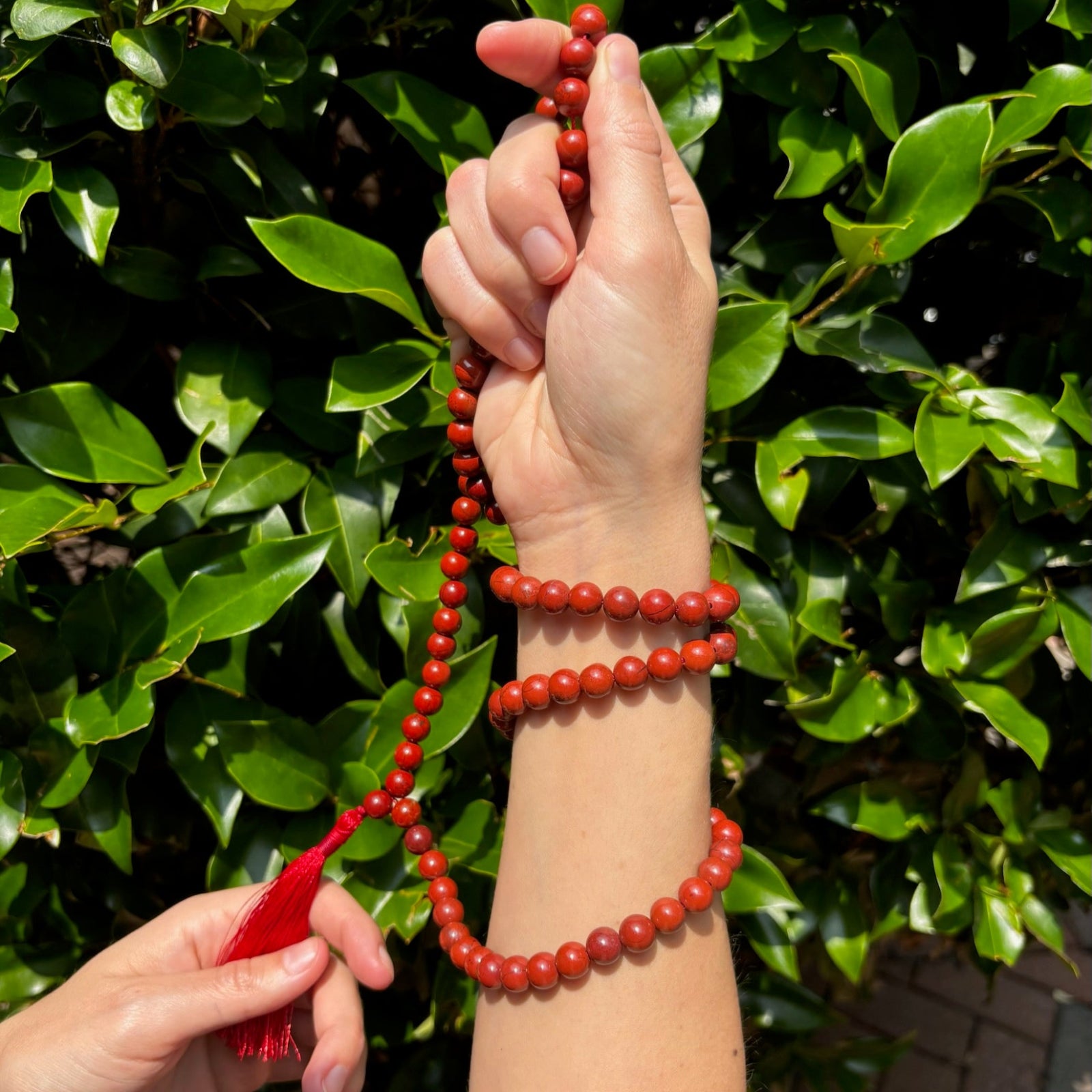 model holding red jasper mala weaved in her hands on a greenery background