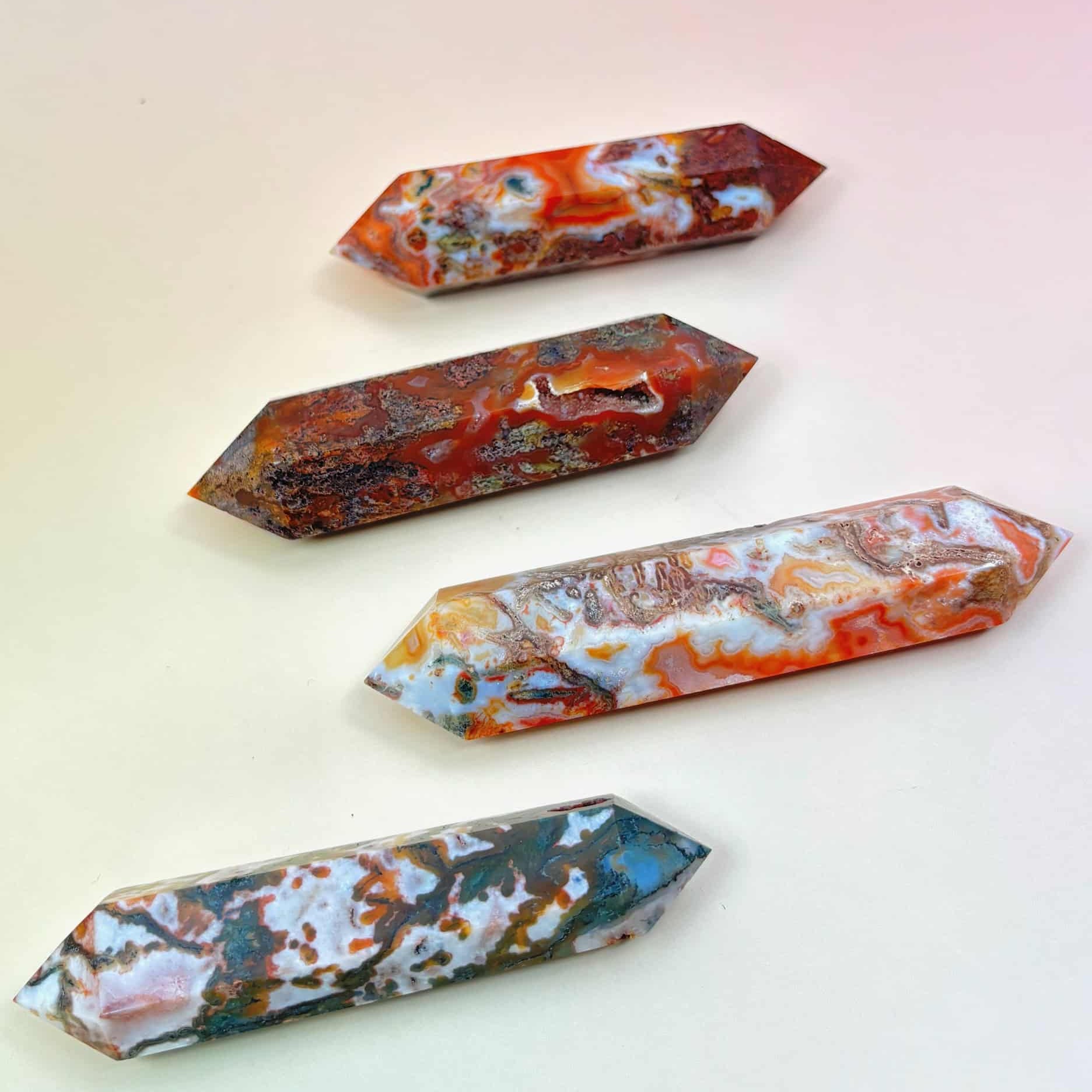 Four polished red moss agate double-terminated points in varying red, green, and white tones on a peach-pink background