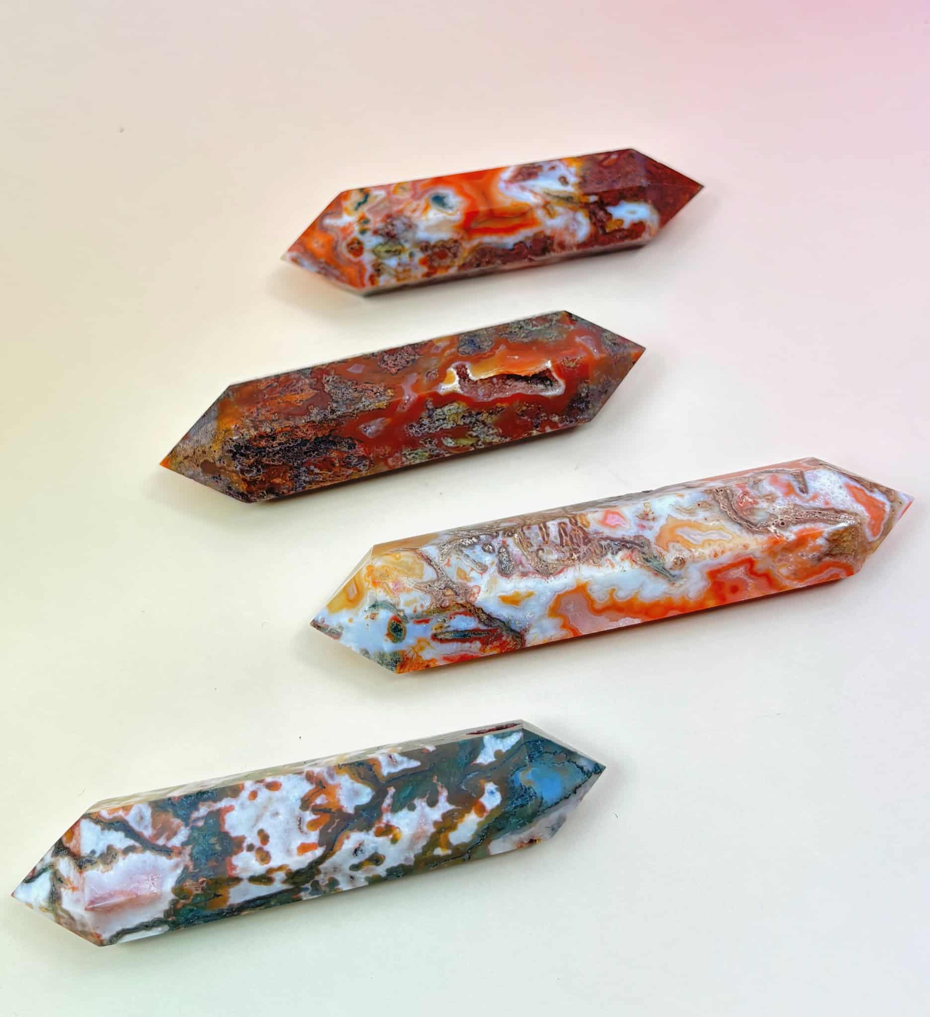 Four polished red moss agate double-terminated points in varying red, green, and white tones on a peach-pink background