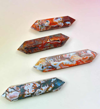 Four polished red moss agate double-terminated points in varying red, green, and white tones on a peach-pink background