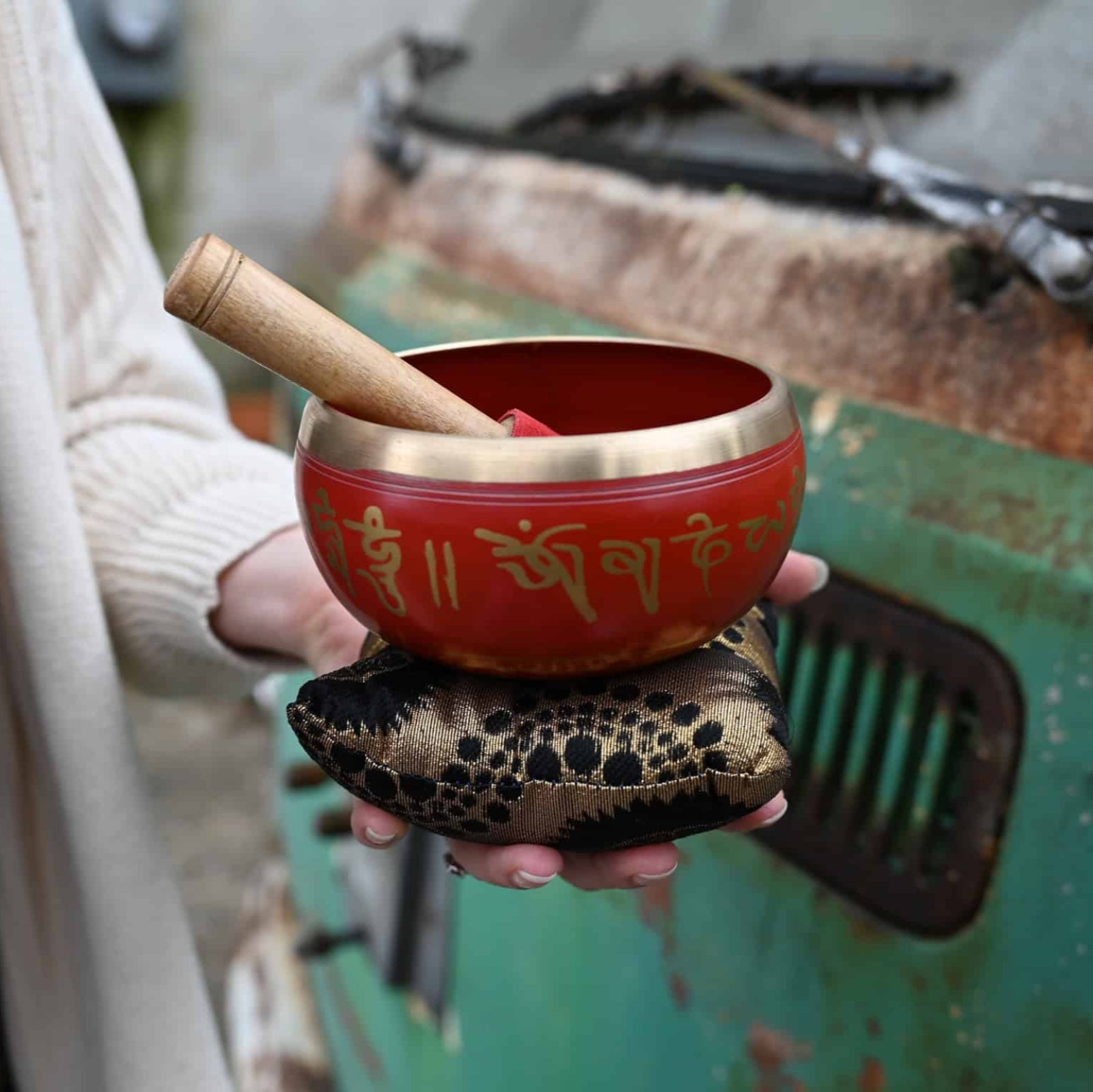 Red singing bowl with gold text held by a person in front of a rustic background