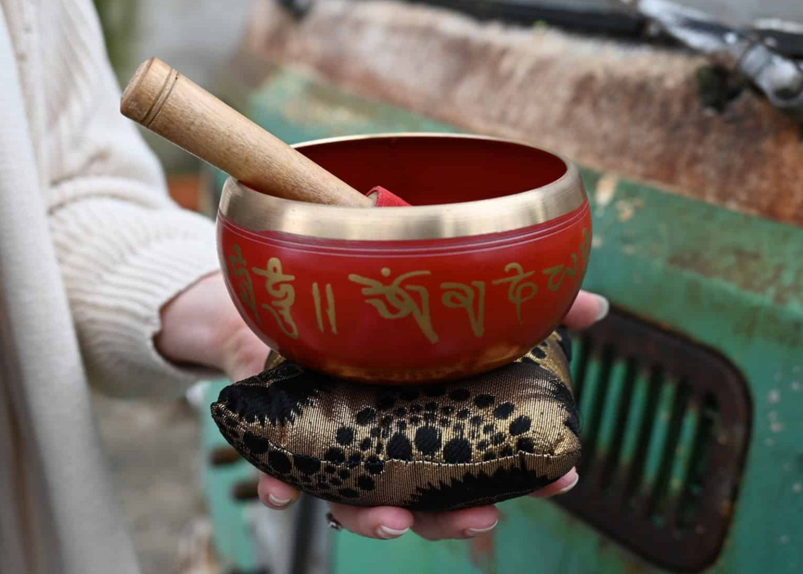 Red singing bowl with gold text held by a person in front of a rustic background