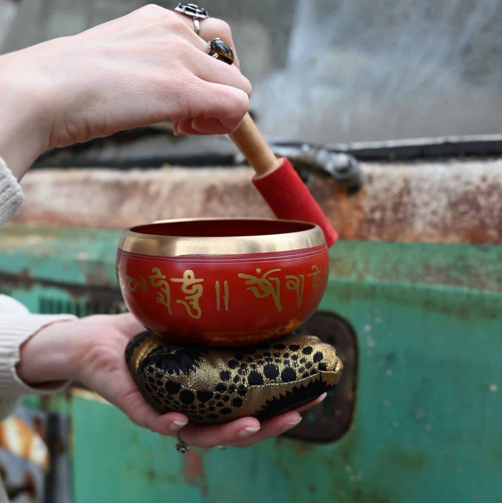 Person holding a red singing bowl with gold designs against a blurred background