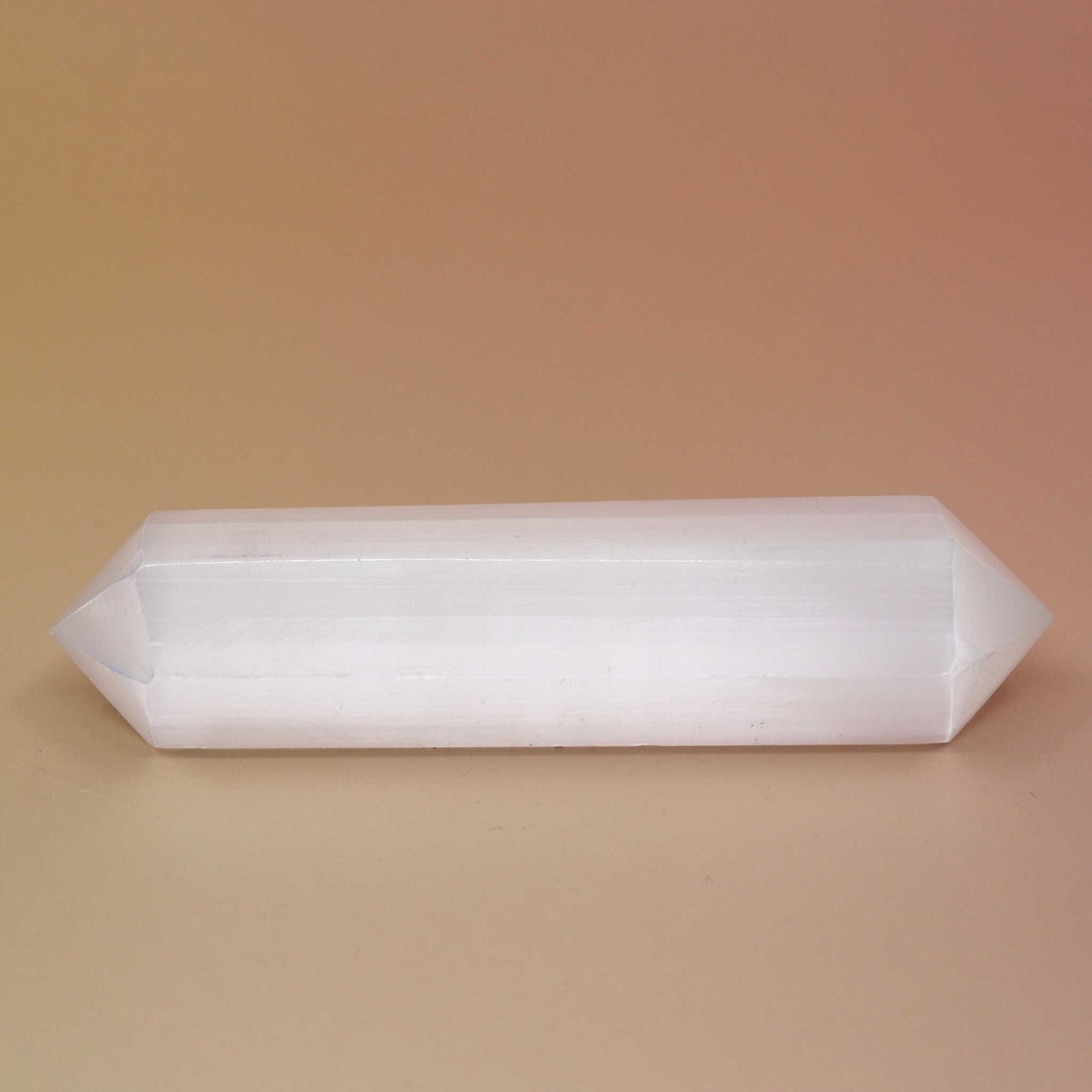 Selenite Crystal Wand on an orange and pink background 