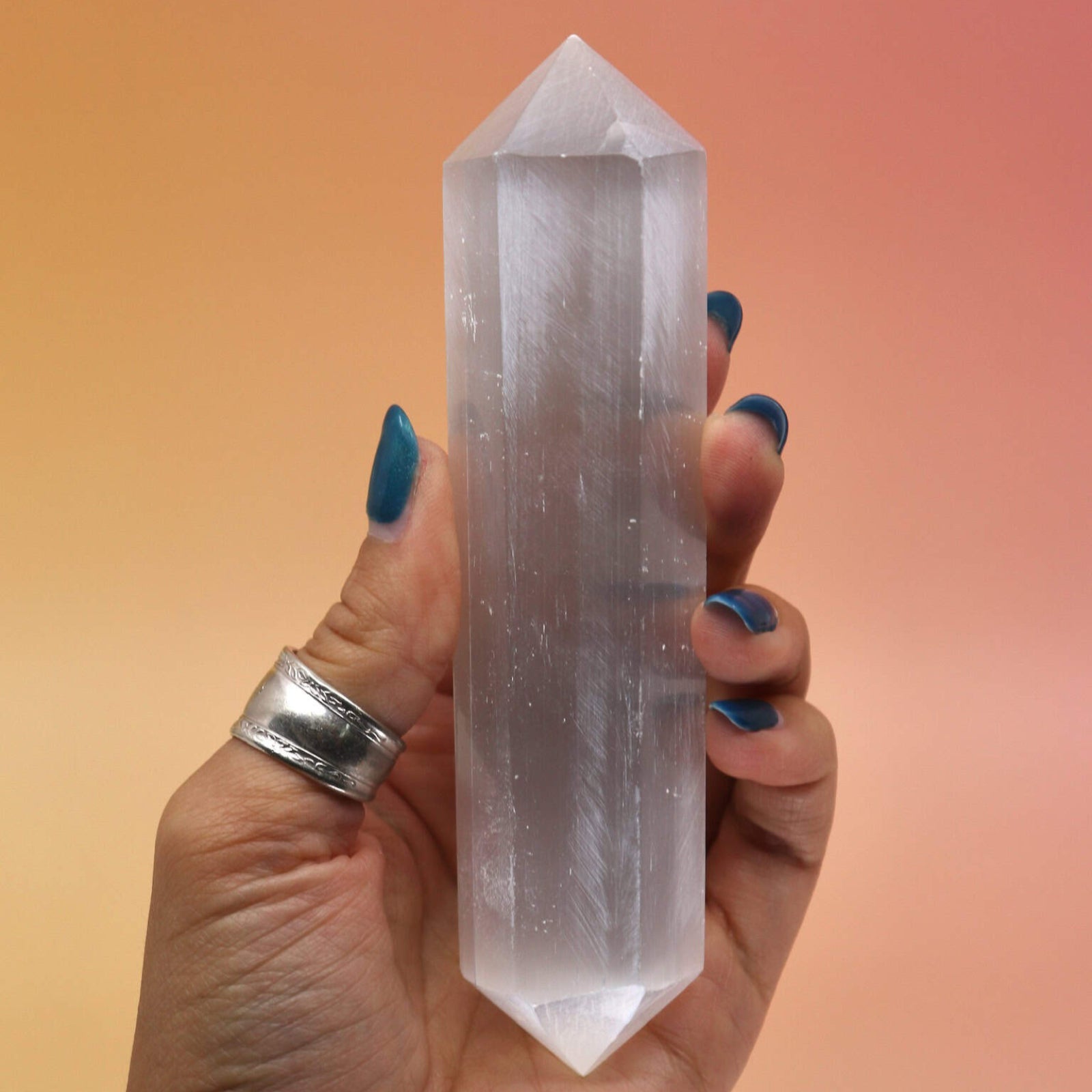 Hand holding a Selenite crystal against a gradient background