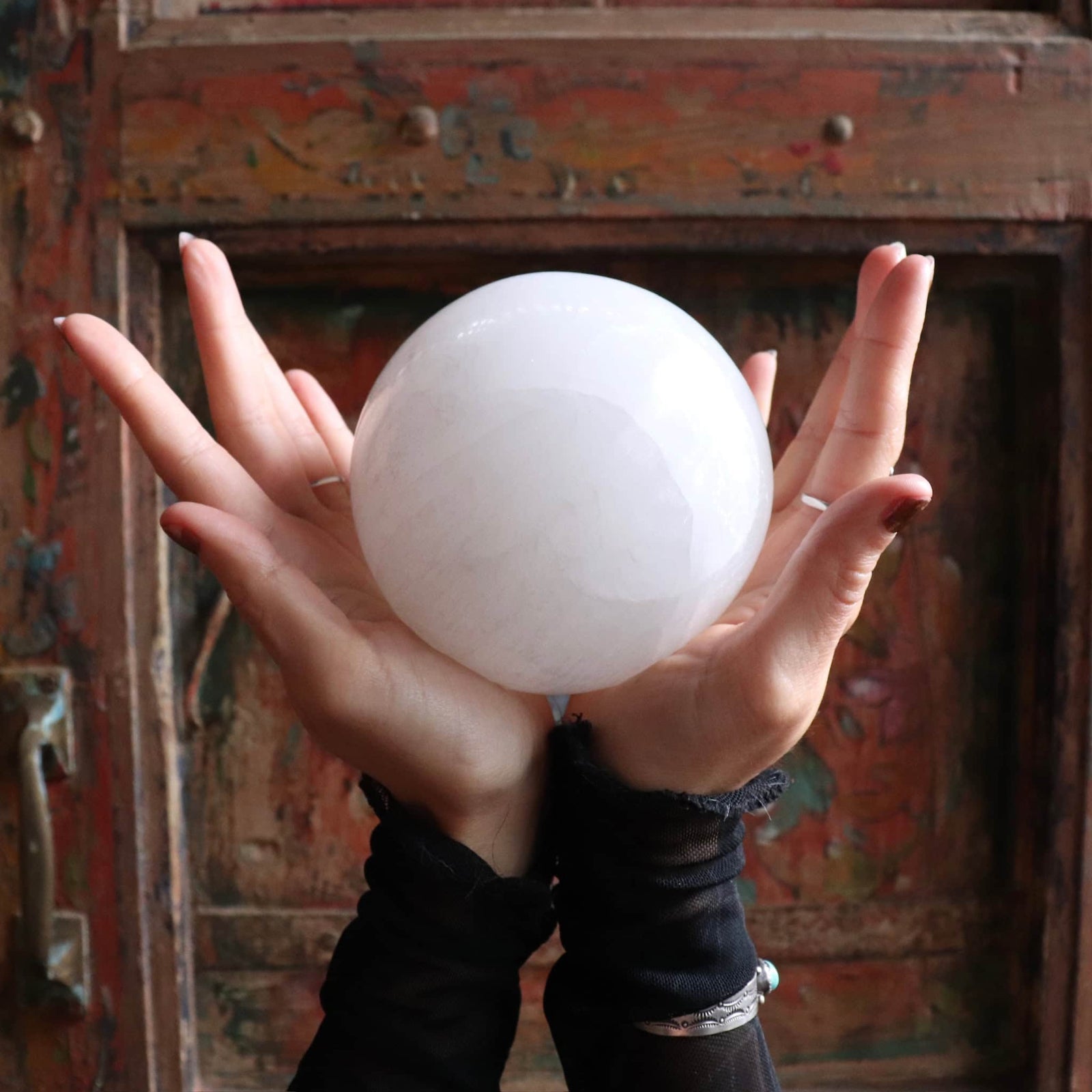 Hands holding a large crystal ball in front of an ornate, colorful background