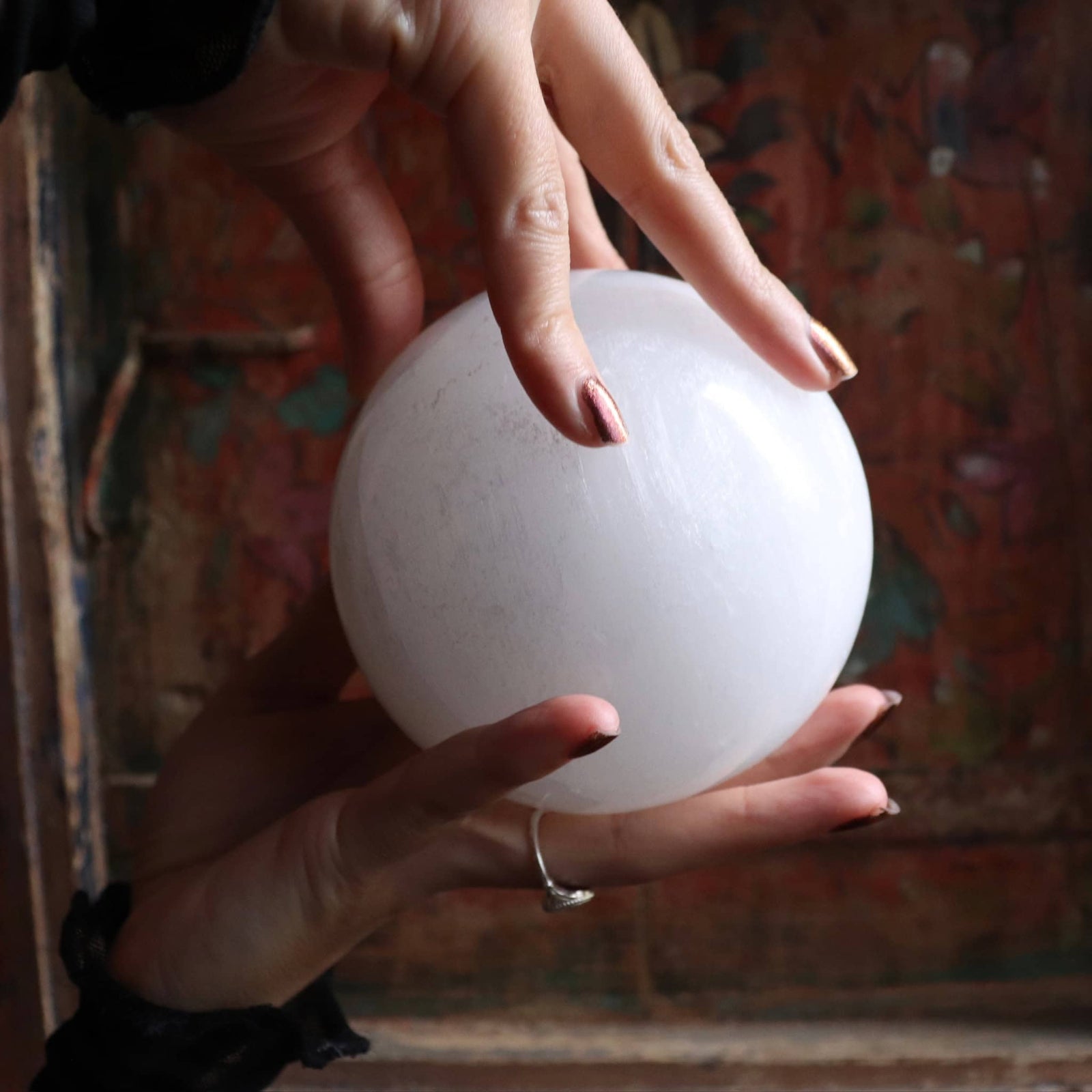 Hand holding a white selenite spherical object against a textured wall background