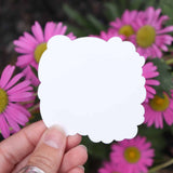 Hand holding a white sticker with pink flowers in the background