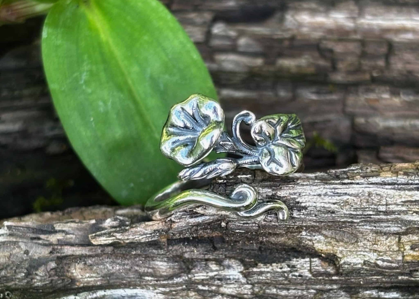 Silver ring with leaf design on a wooden surface with green leaves