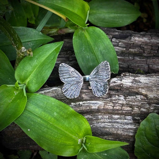 Silver Butterfly-shaped ring on a wooden log with green leaves