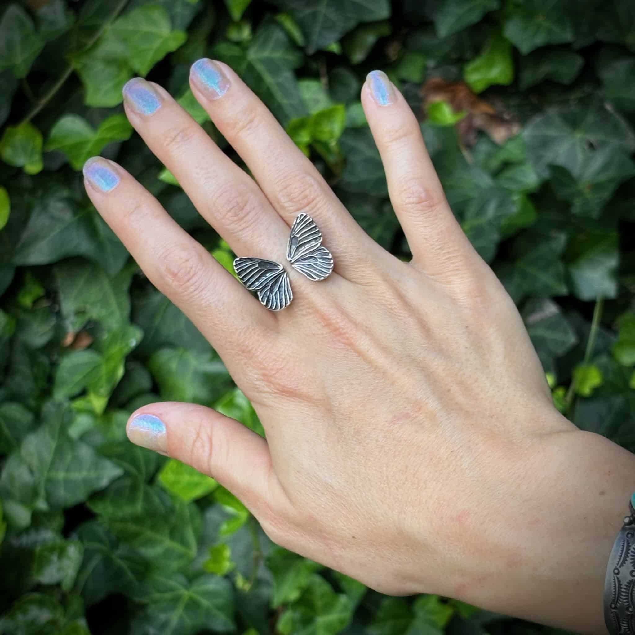 Hand wearing a sterling silver butterfly ring with a green leafy background