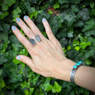 Hand wearing a silver ring and bracelet with turquoise stones against a green leafy background