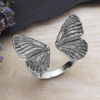 Silver butterfly wing ring on a wooden surface with dried flowers.