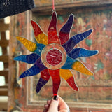 Colorful stained glass sunflower decoration held by a hand with a blurred background
