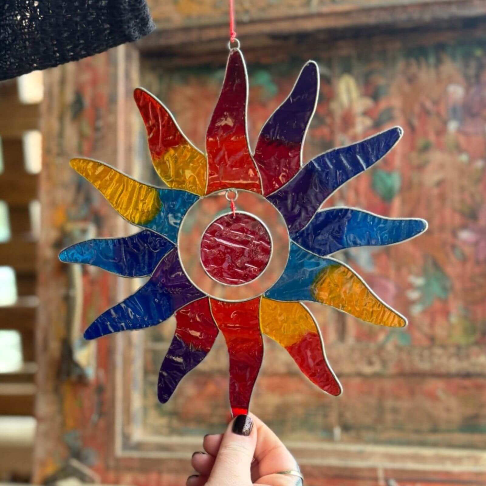 Colorful stained glass sunflower decoration held by a hand with a blurred background