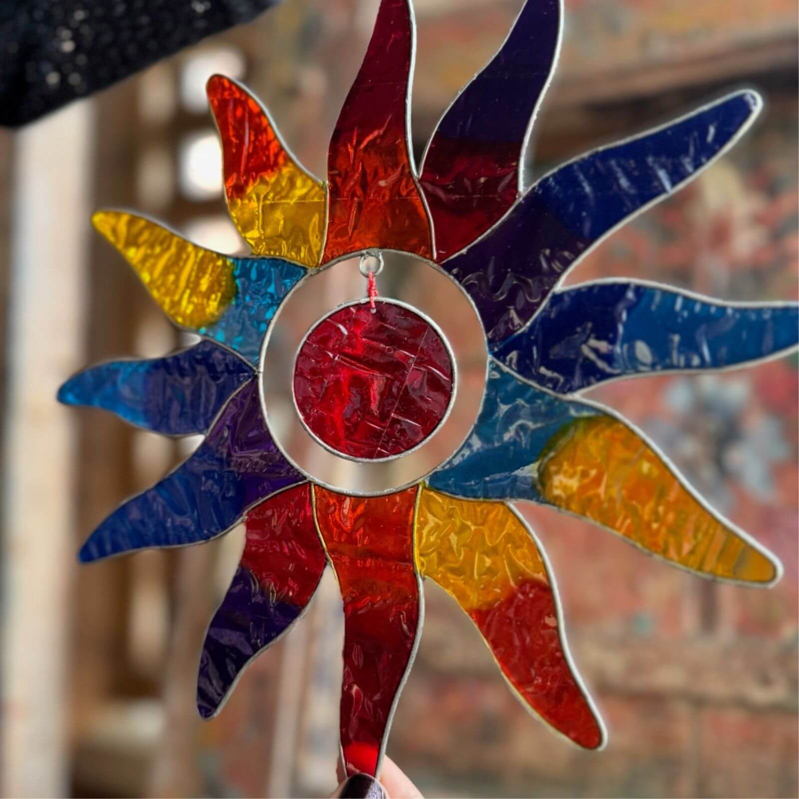 Colorful sun-shaped stained glass window hanging with a blurred background