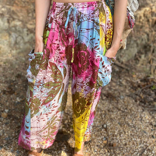 Rainbow tie-dye cargo pants with green floral moth pattern with hands in pocket