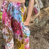Rainbow tie-dye cargo pants with green floral moth pattern close up view with hand in pocket