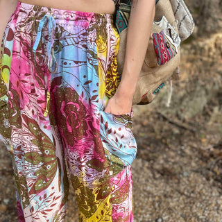 Rainbow tie-dye cargo pants with green floral moth pattern close up view with hand in pocket