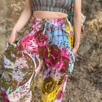 Rainbow tie-dye cargo pants with green floral moth pattern close up view with expanded hands in pockets