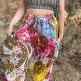 Rainbow tie-dye cargo pants with green floral moth pattern close up view with expanded hands in pockets