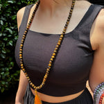 model wearing a black tank top in front of greenery with a tiger eye mala around her neck