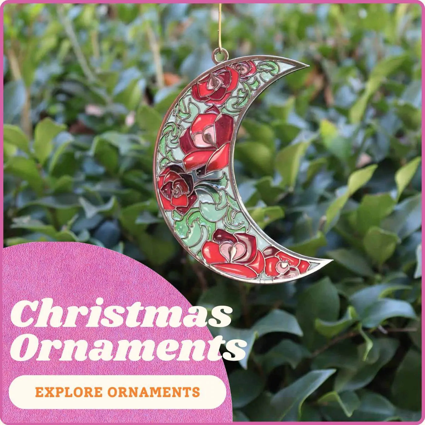 Decorative crescent ornament with red and green design hanging against a green leafy background.